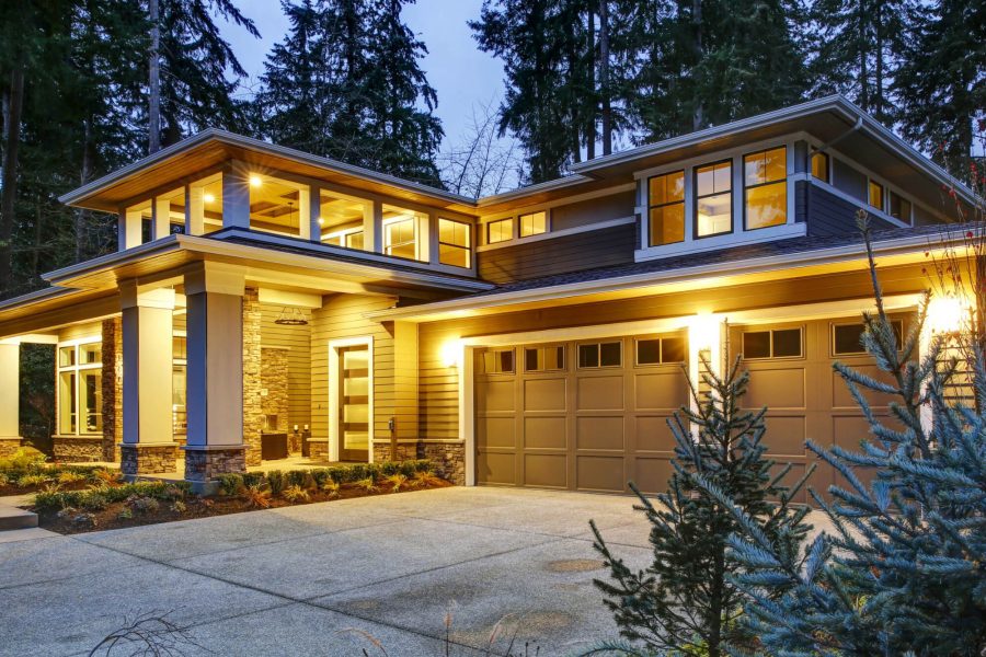 Luxurious new construction home exterior at sunset. View of two garage spaces with concrete driveway and illuminated porch with columns.